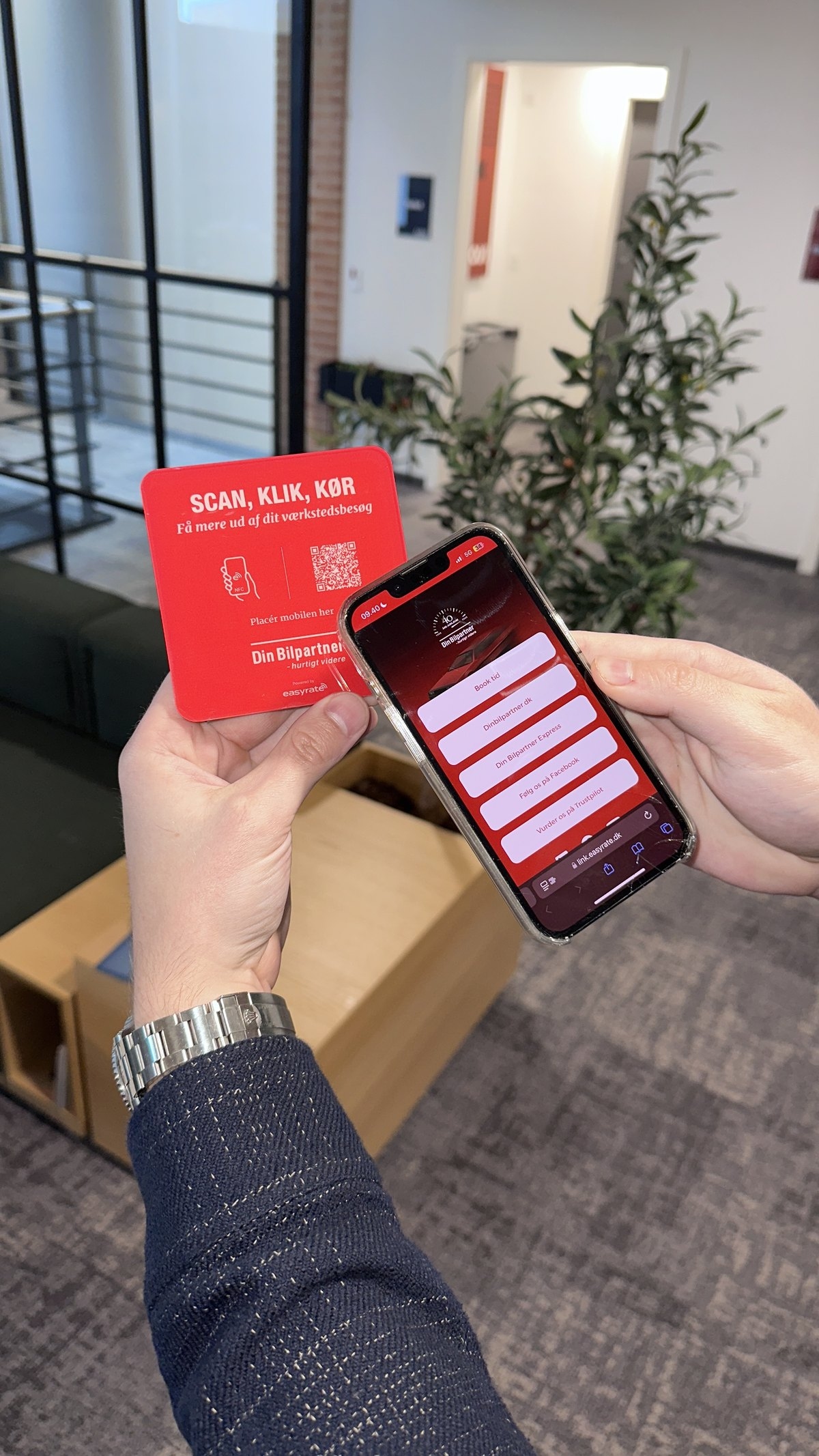 Hånd med rød Din Bilpartner NFC-plade og en mobil, der viser værkstedets easylink